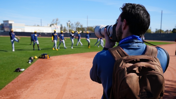 Journalism student taking photos of players on a baseball field.