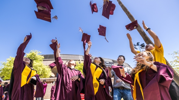 Group of graduates in maroon caps and gowns through their caps into the air