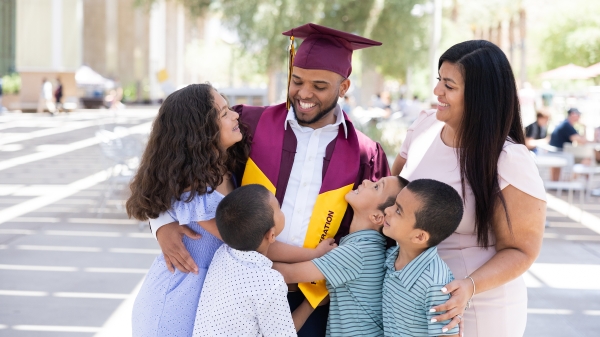 A mom and four little kids hug their dad in ASU graduation gear