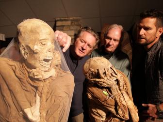 three men looking at two mummies