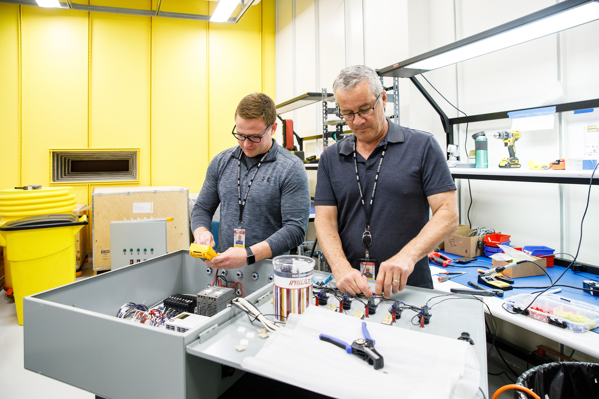 Two men work with electrical equipment in a lab. The caption reads: Mechanical engineering student Alex Gardeck and engineer Steve Rednour work on an electrical control panel of the Compact X-ray Free Electron Laser.