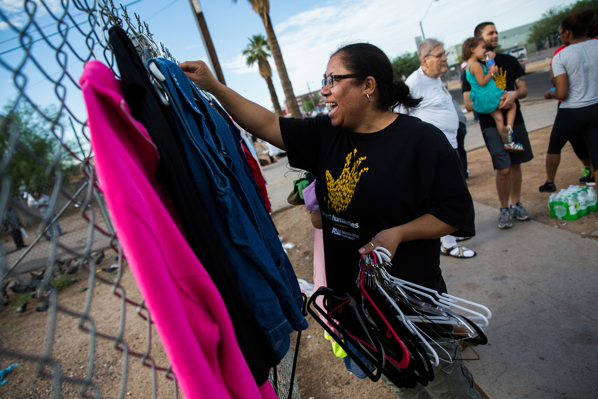 A woman smiles as she takes shirts and hangers off a fence