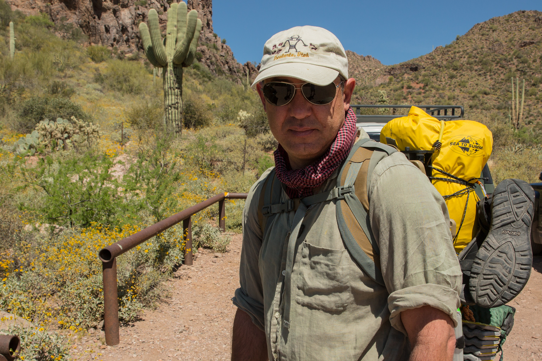 A man wearing a backpack and hiking gear pauses for a photo on a trail