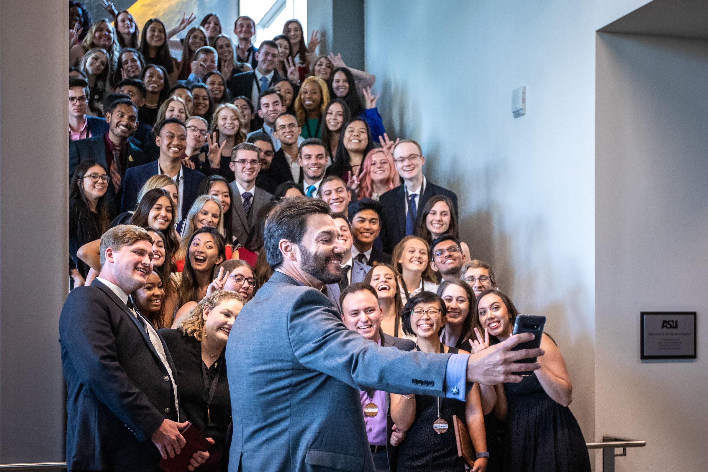 Dean Jonathan Koppell takes a group selfie in front of a staircase packed with Next Generation Service Corps students