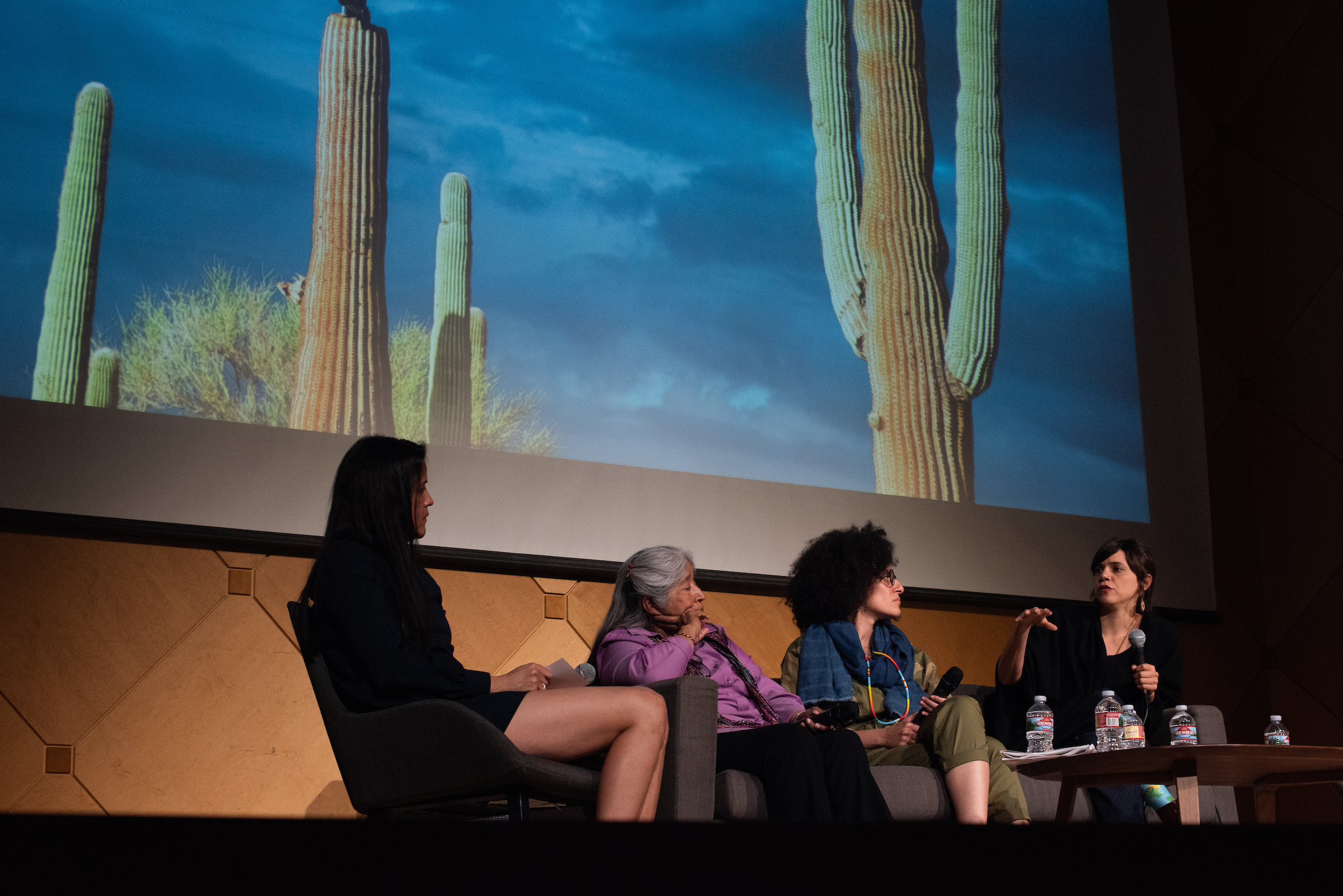 four women sitting and talking on a stage with a photo of cacti in the background