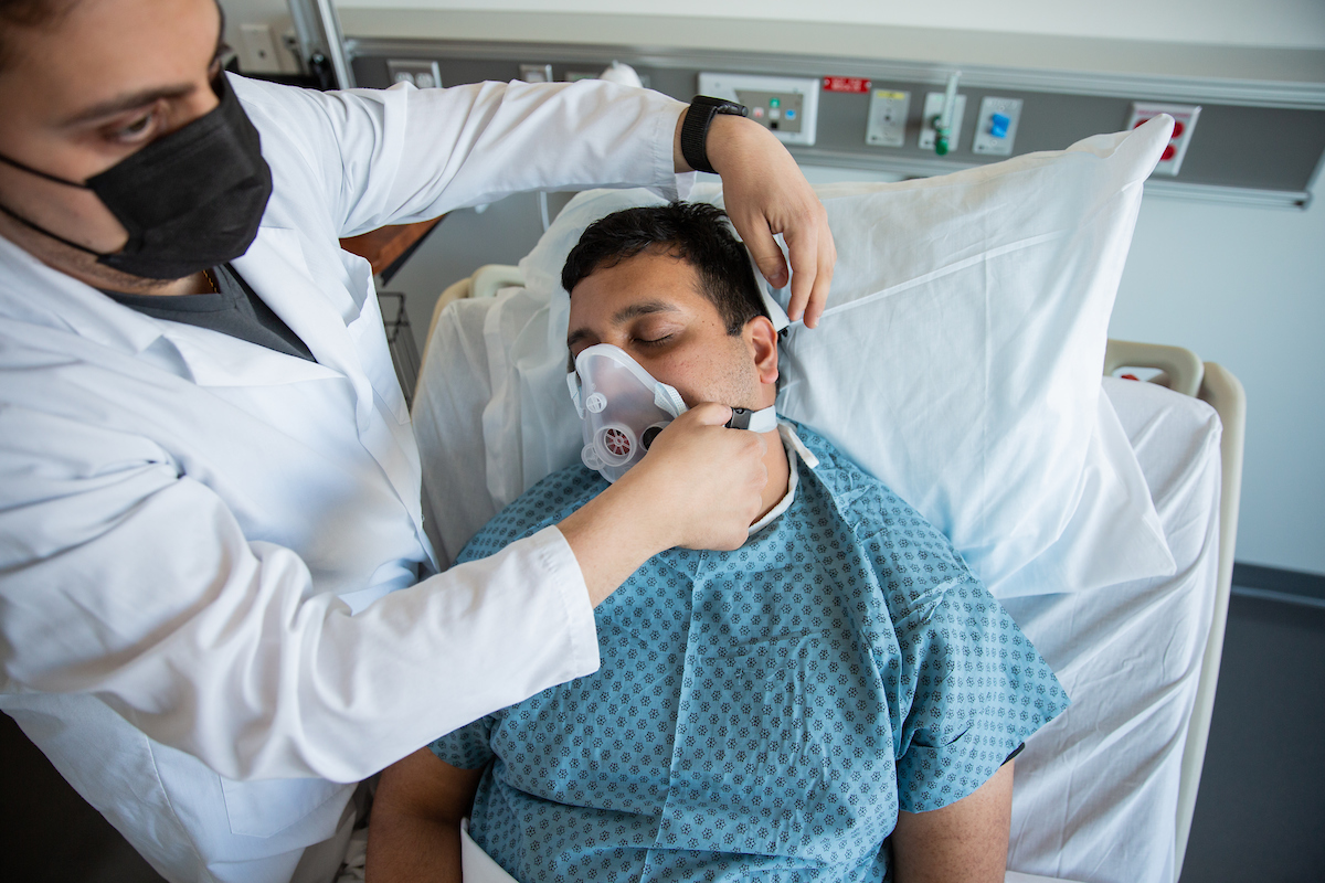 A person wearing a medical mask attaches a breathing mouthpiece to a patient in a simulation