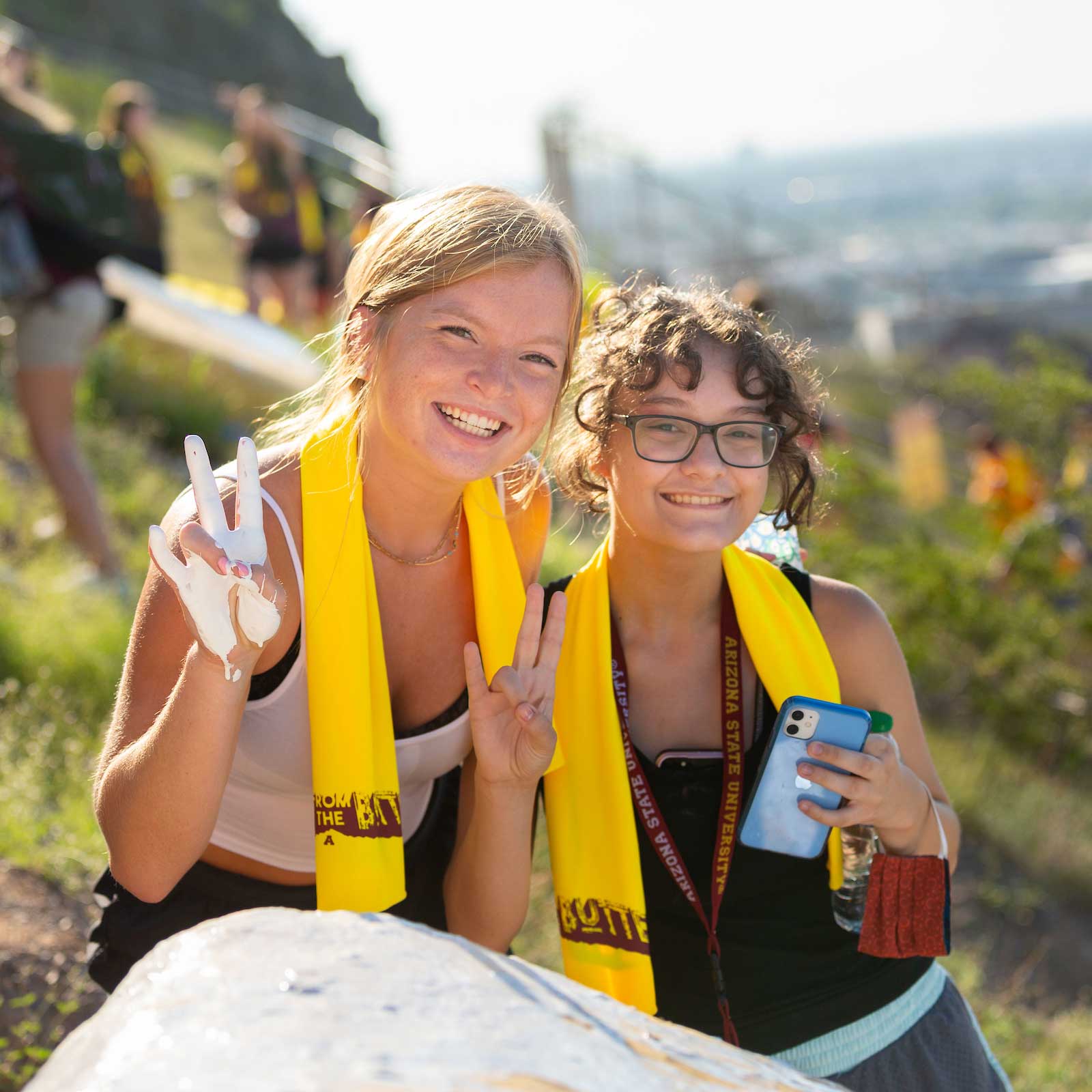 Two young women hold up white-painted hands in the ASU pitchfork gesture