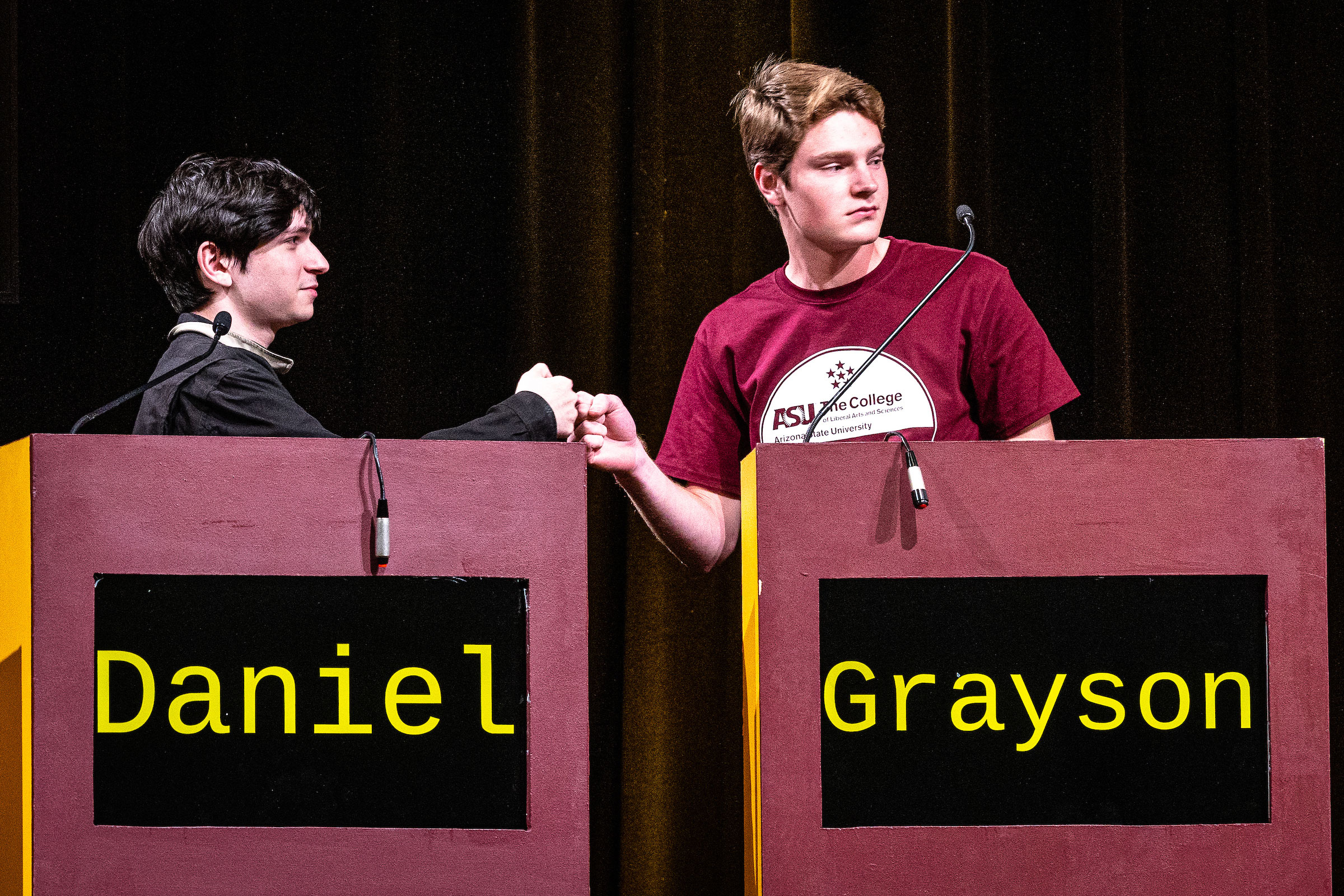 Two students fist-bump while standing behind lecterns.