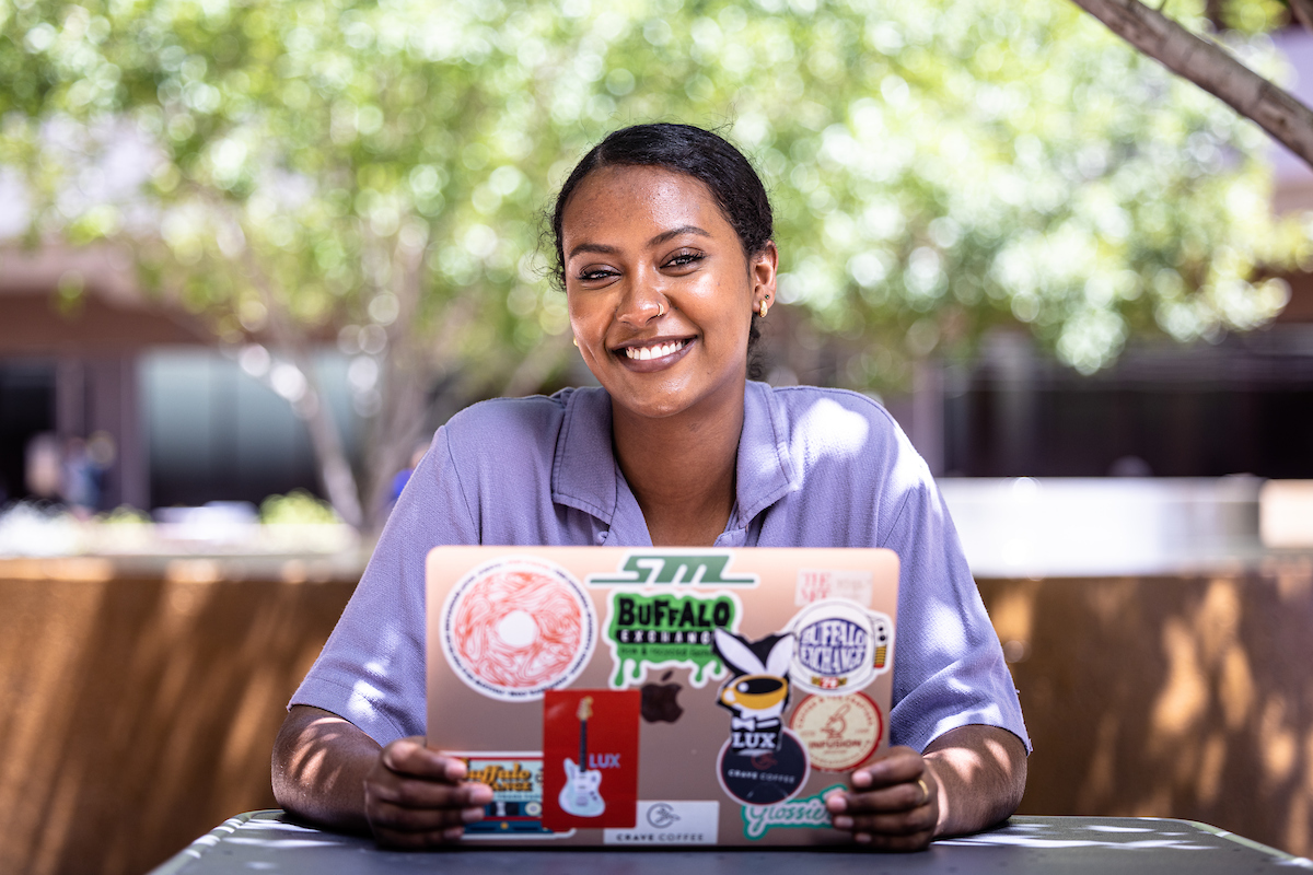 , a student at ASU's Barrett, The Honors College, smiling while seated at a picnic table with a laptop.