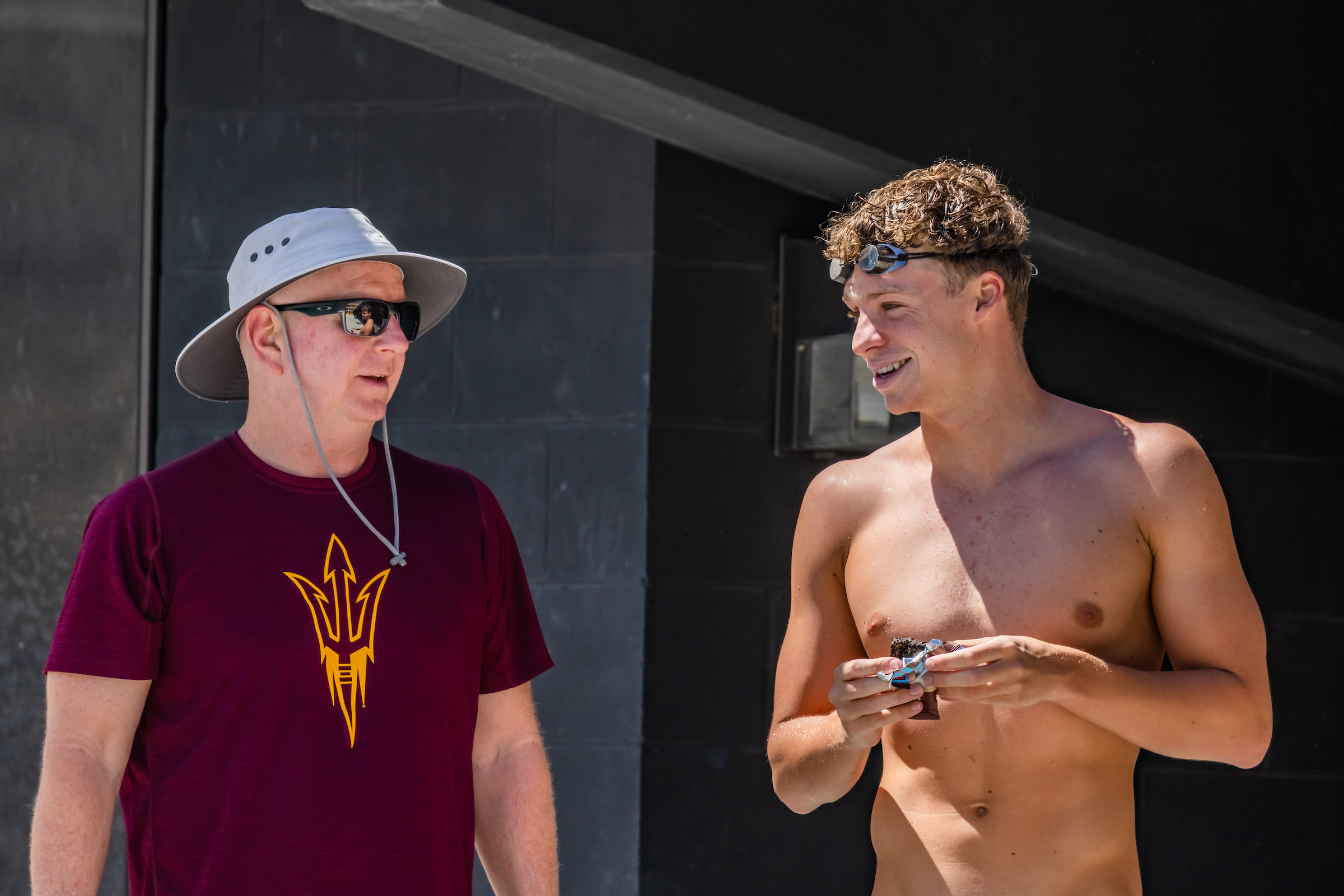 ASU swim coach and collage male swimmer standing outside of pool