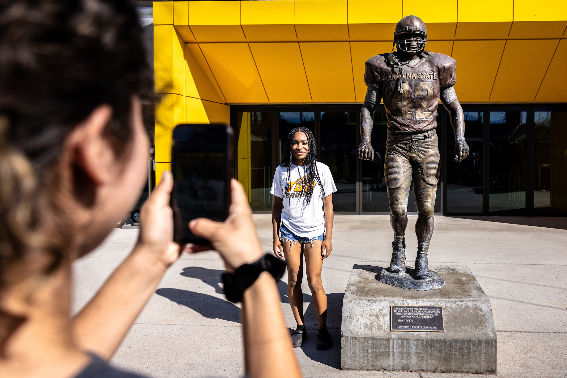High school student taking a picture of her friend next to ASU's Pat Tillman statue