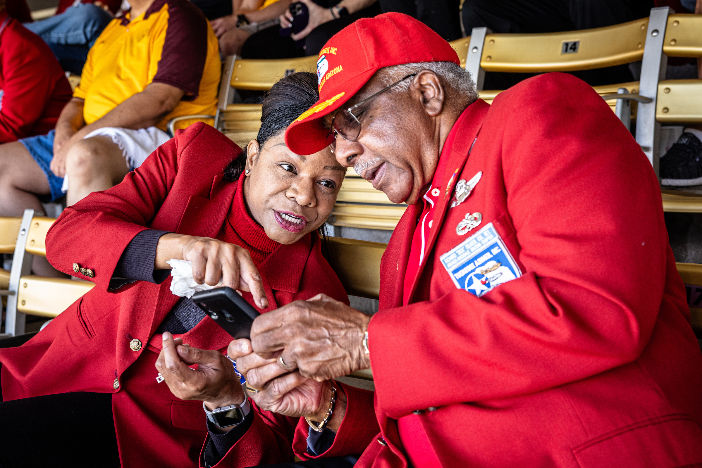 A woman shows her phone to a man in stadium seats