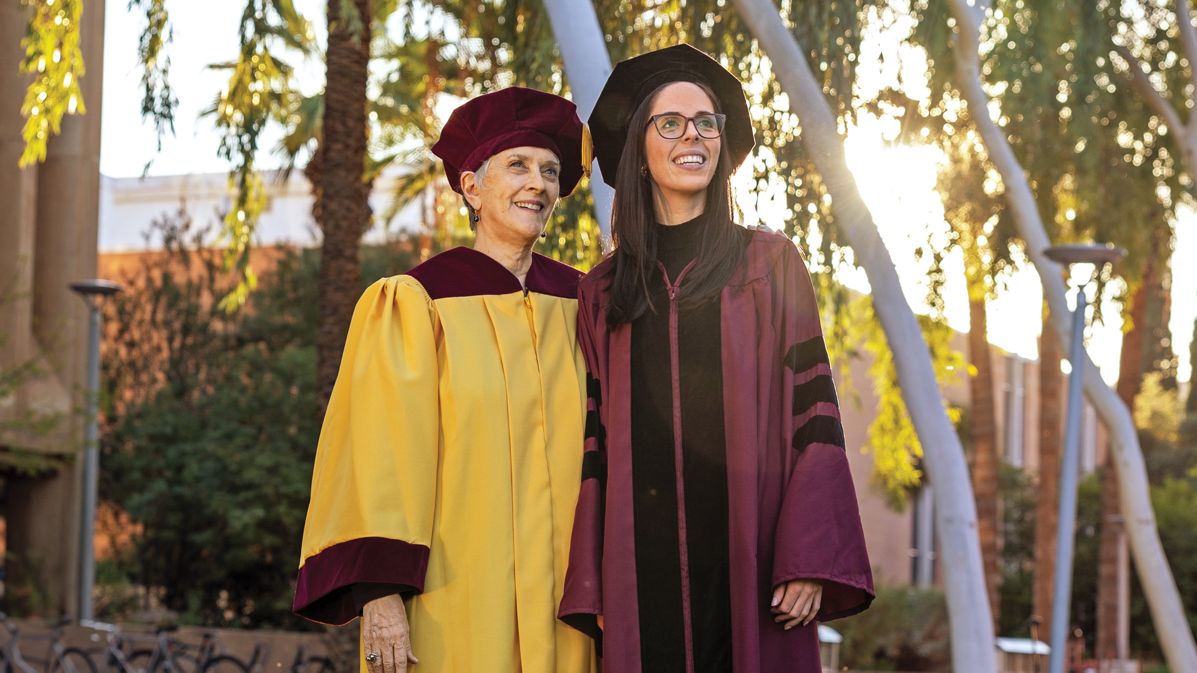 Two people posing in gold and maroon graduation robes