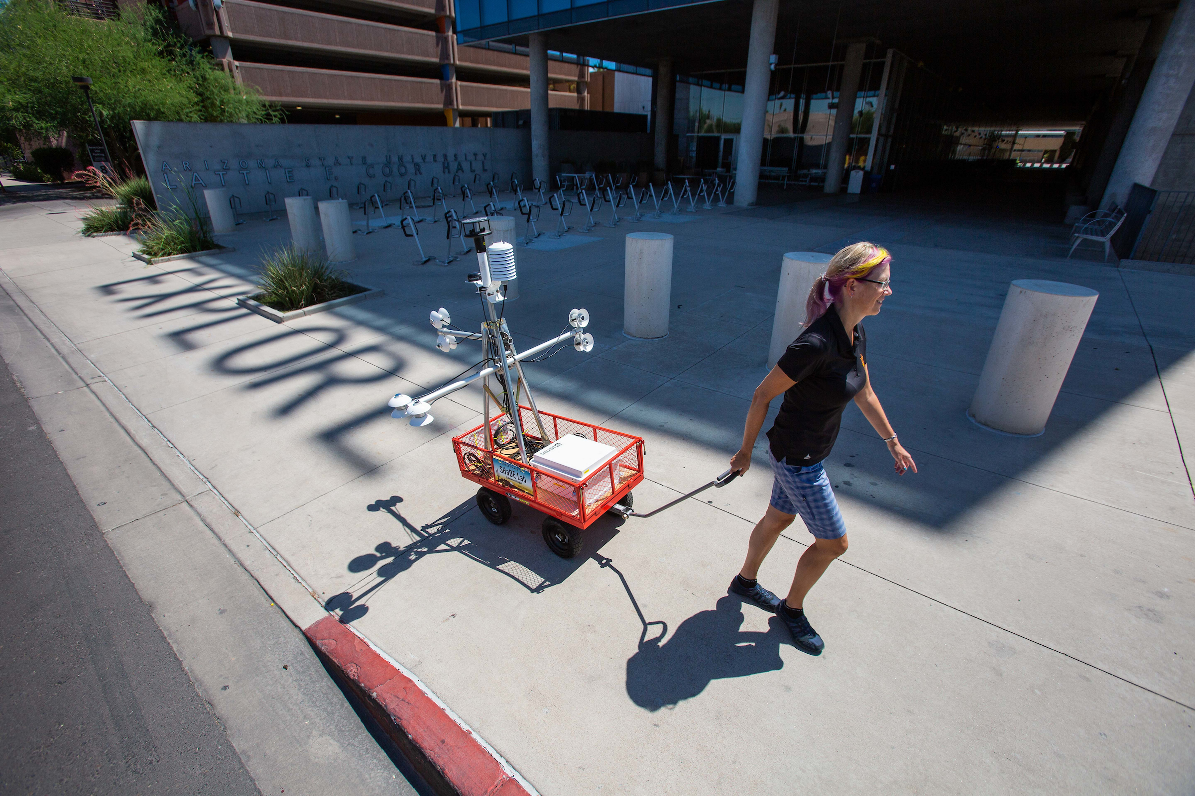 Woman pulling heat-measuring robot cart along a sidewalk