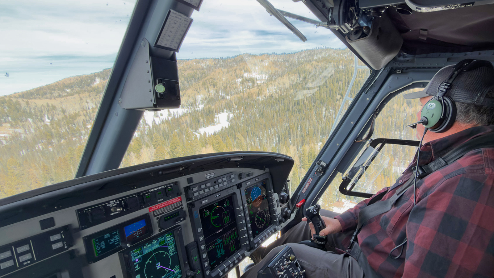 A man pilots an aircraft over a forested area.