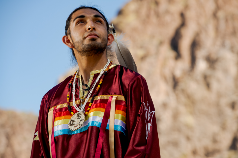 Indigenous man from Arizona wearing tribal regalia standing in front of a man