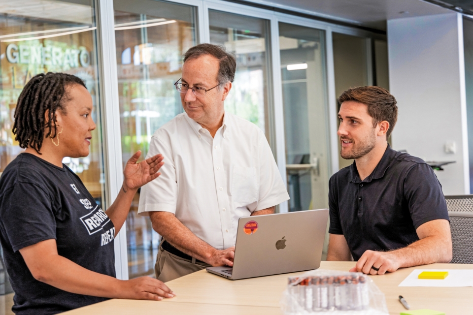 Three people talk at table in lab