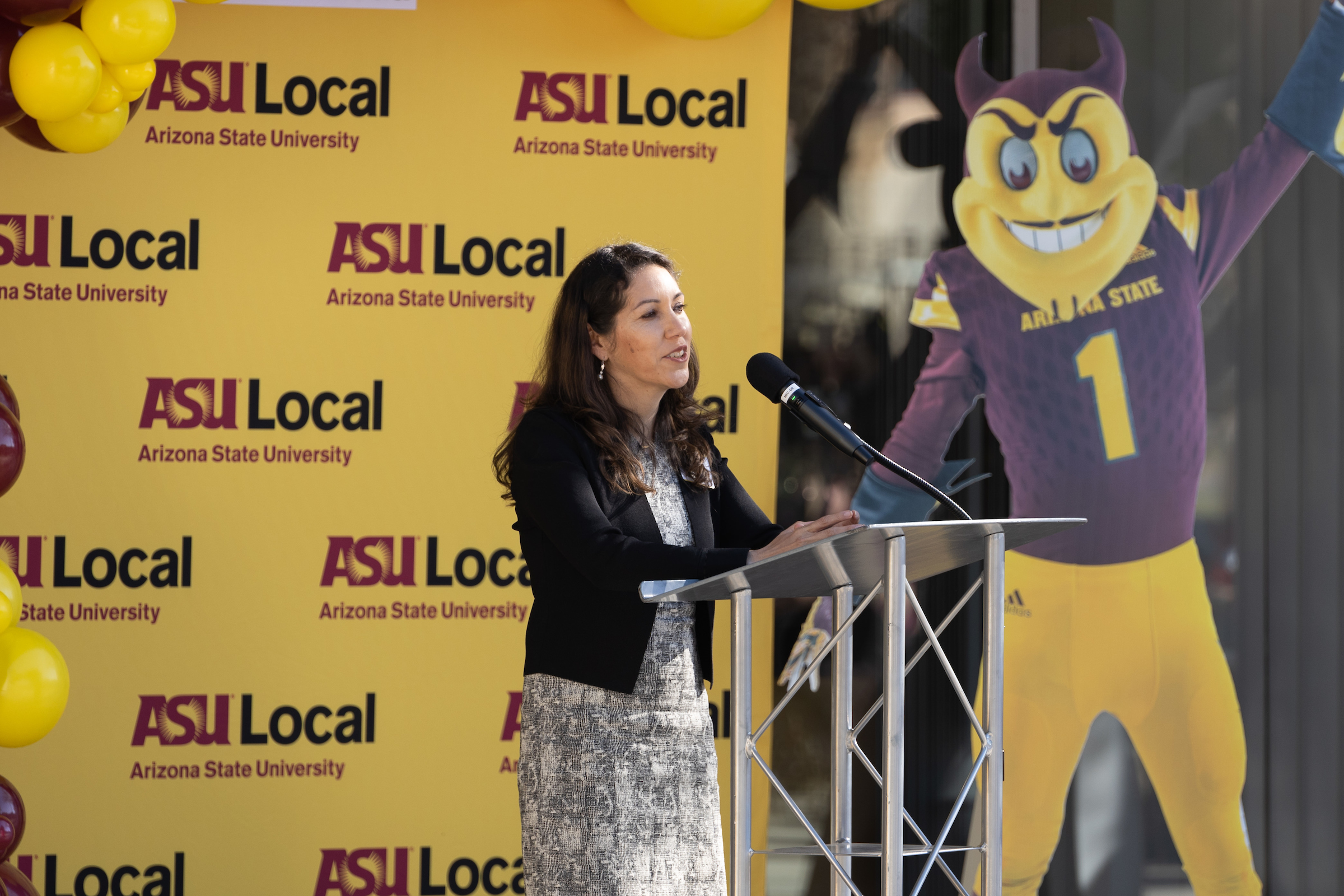 woman speaking at lectern at ASU Local event with cardboard cutout of Sparky mascot in background