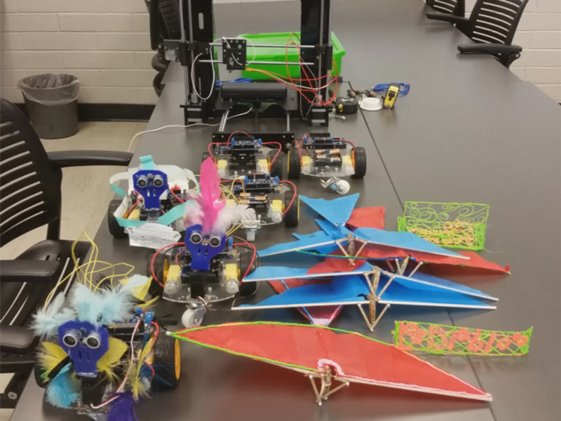 Bird toys and robotic cars rest on a table for an outreach program.