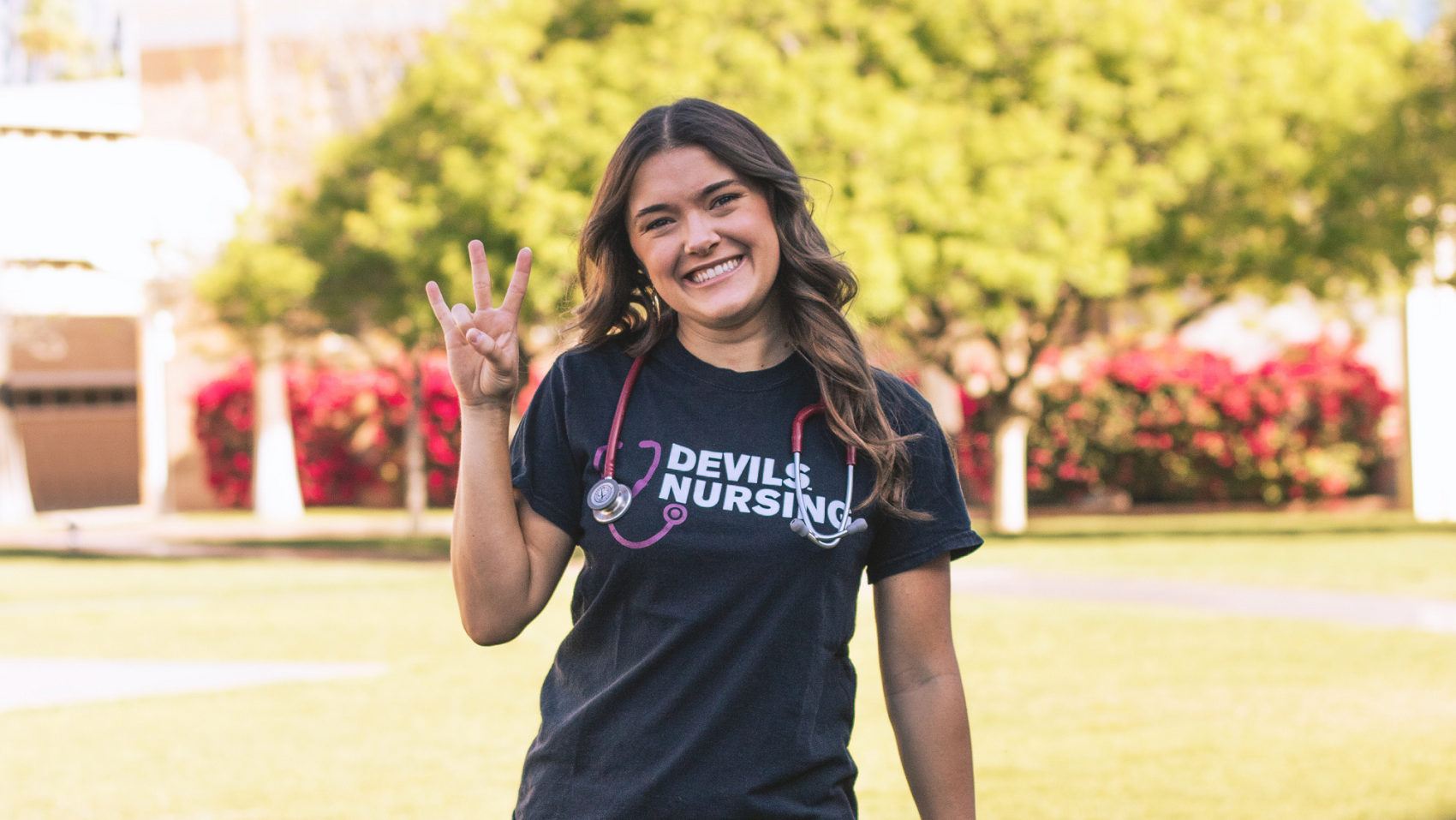  Smiles at the camera with a stethoscope around her neck while throwing a pitchfork. She is wearing a black shirt that says Devils Nursing on it. 