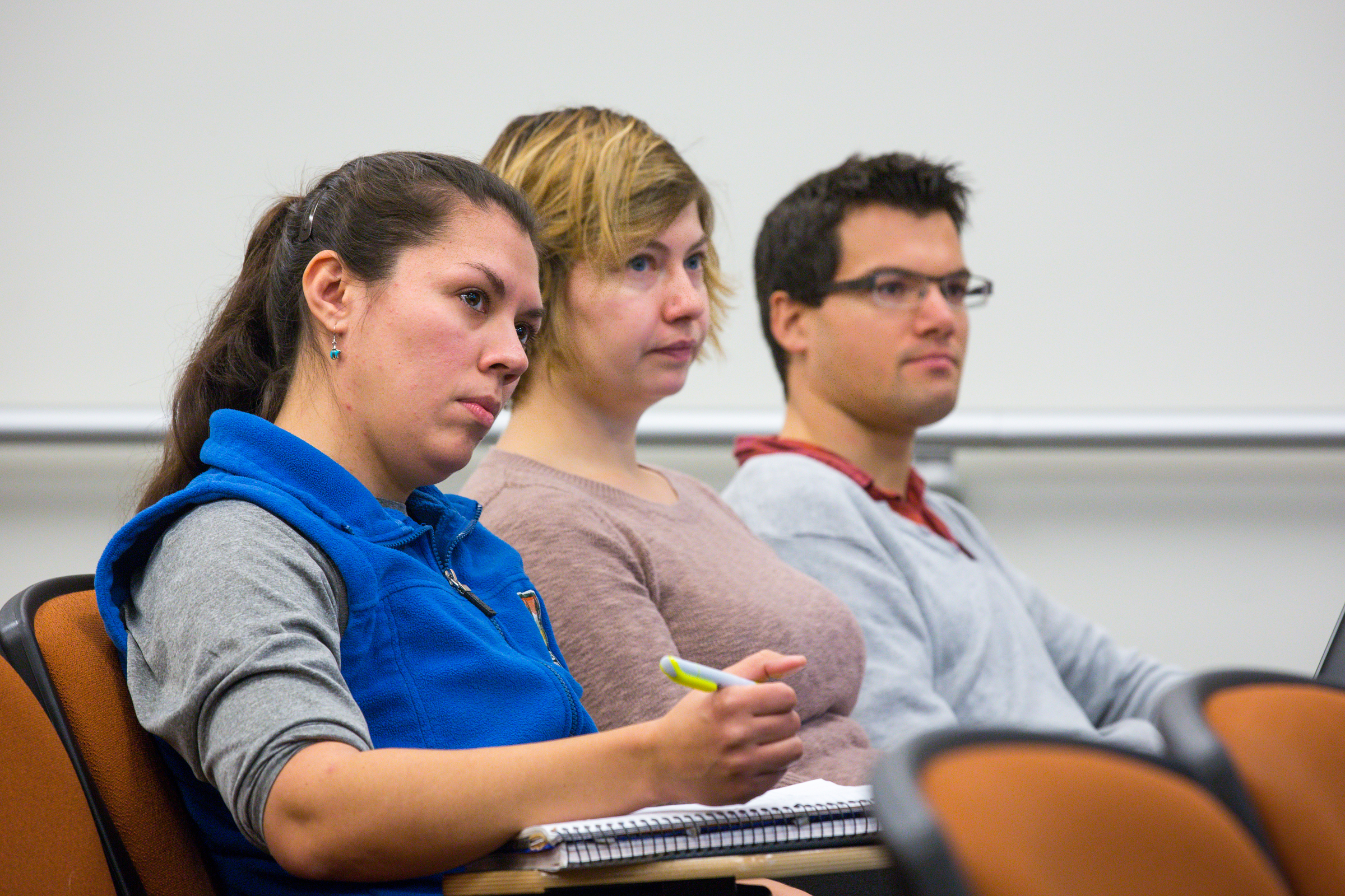 Three students sit in a classroom listening to a presentation.