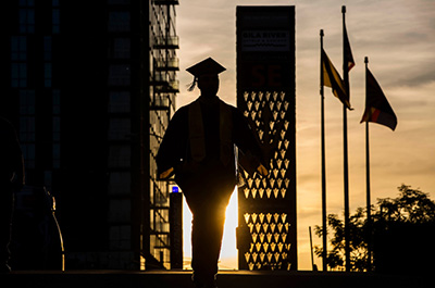 graduate in cap and gown silhouette by sunset