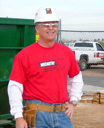 A man stands at a construction site with a construction hat and tool belt
