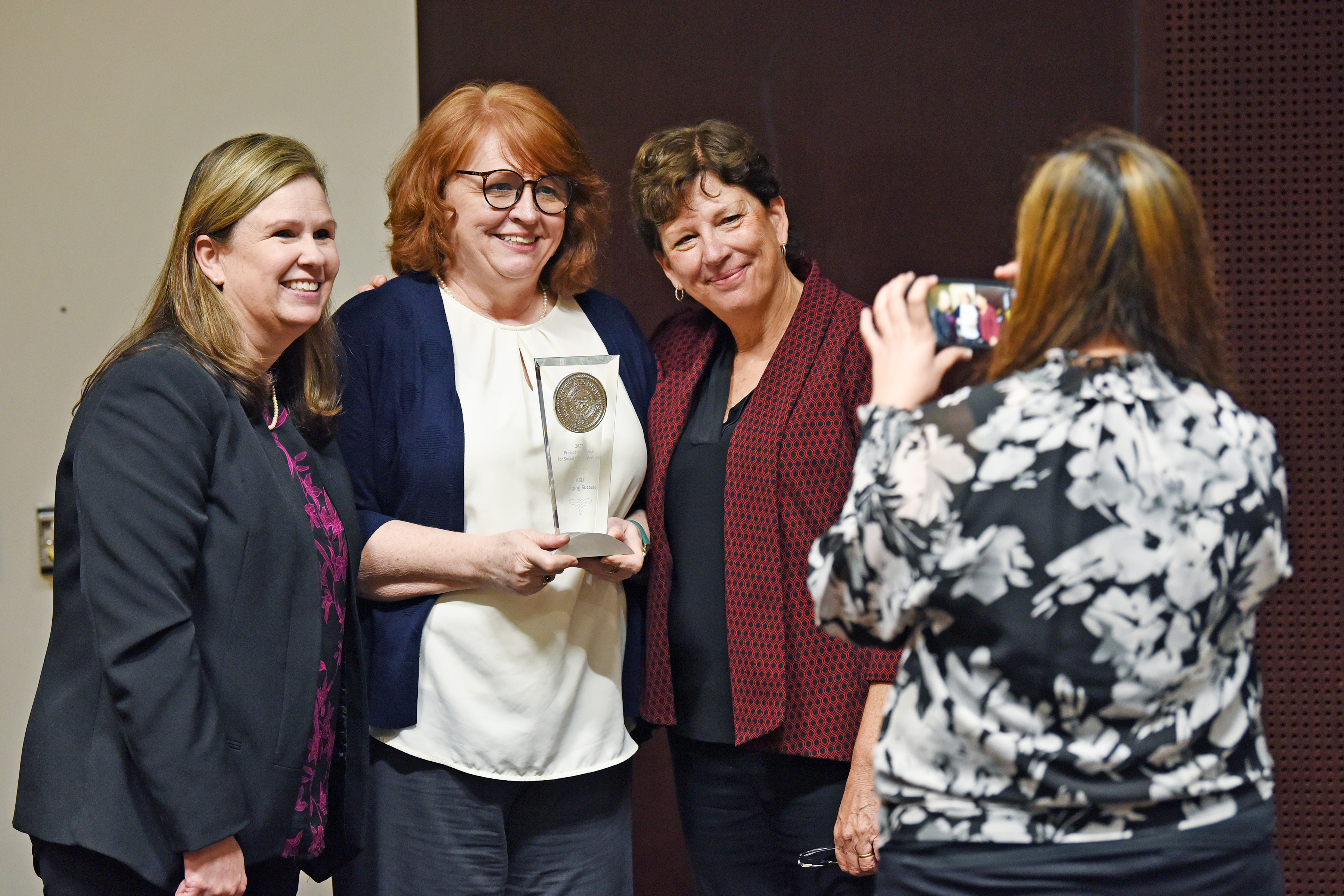 Woman taking picture of group with award