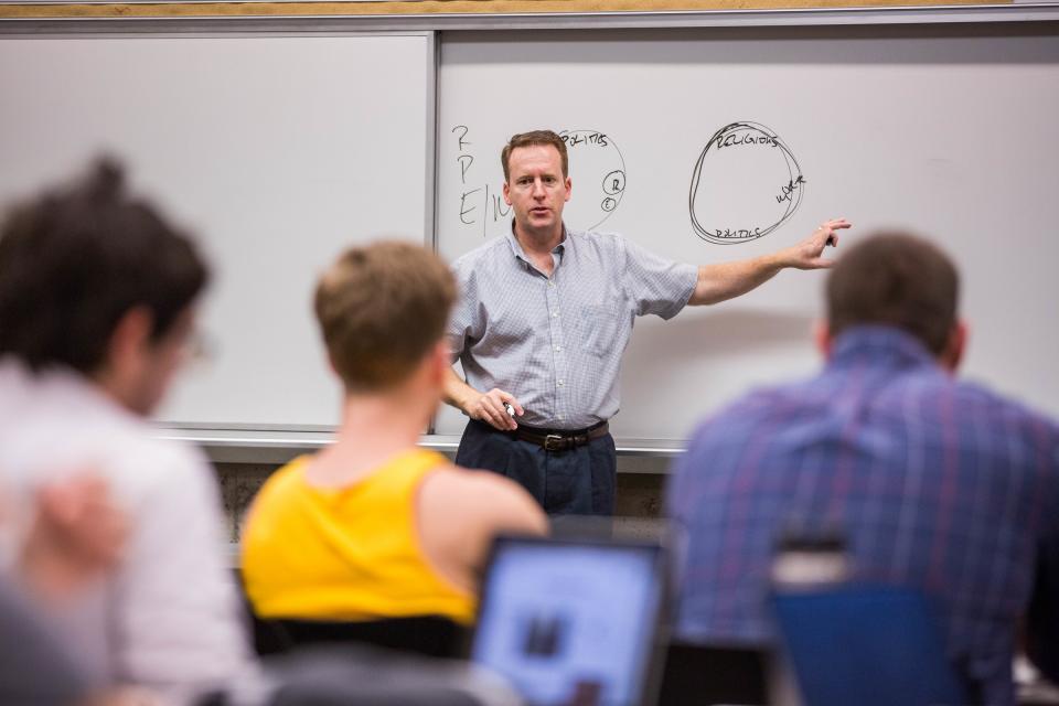 man at front of classroom pointing to whiteboard