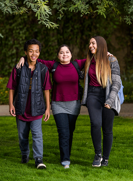 Three high schoolers walk arm-in-arm