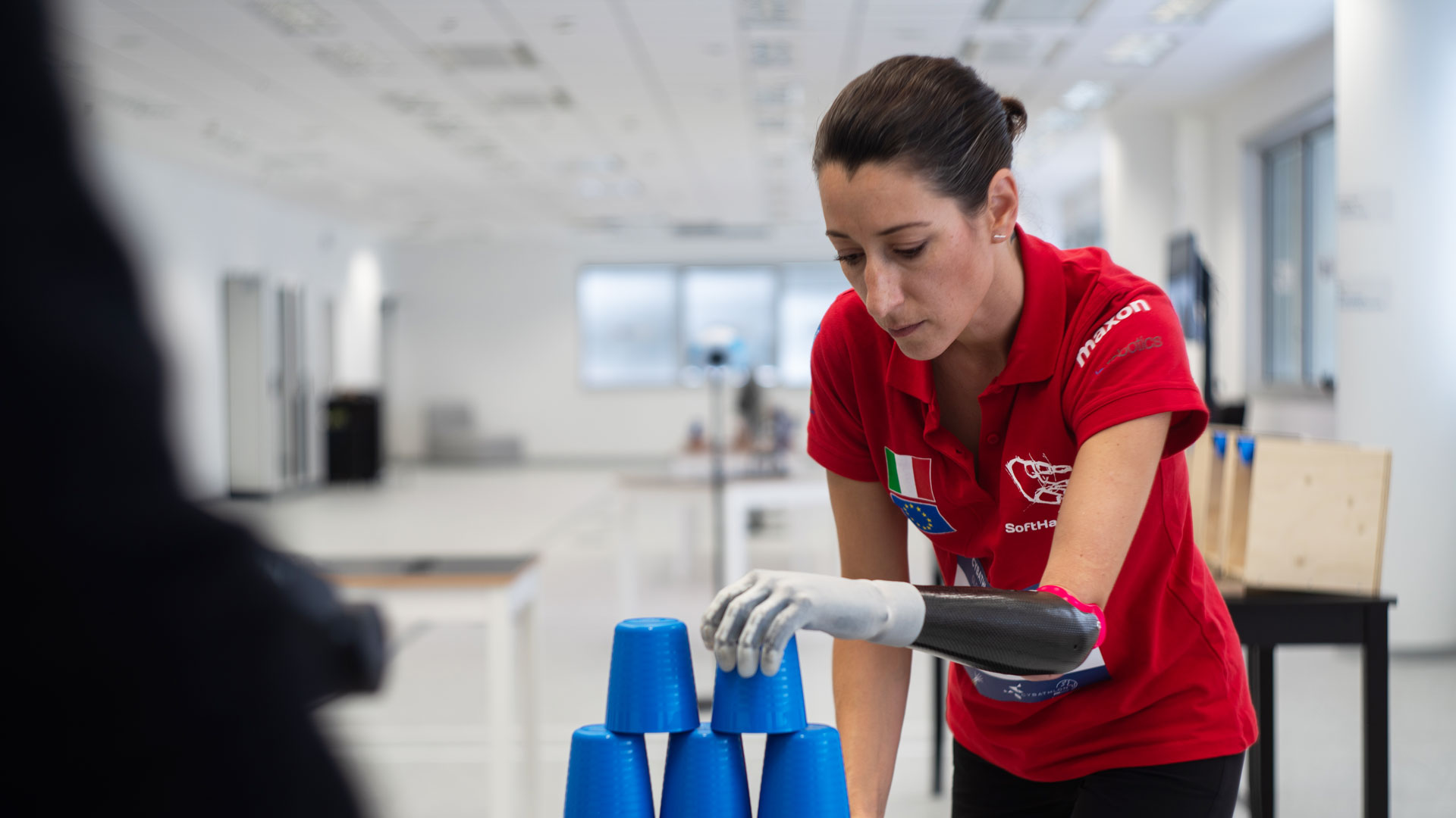 Maria Fossati using the SoftHand Pro prosthetic hand to stack cups.