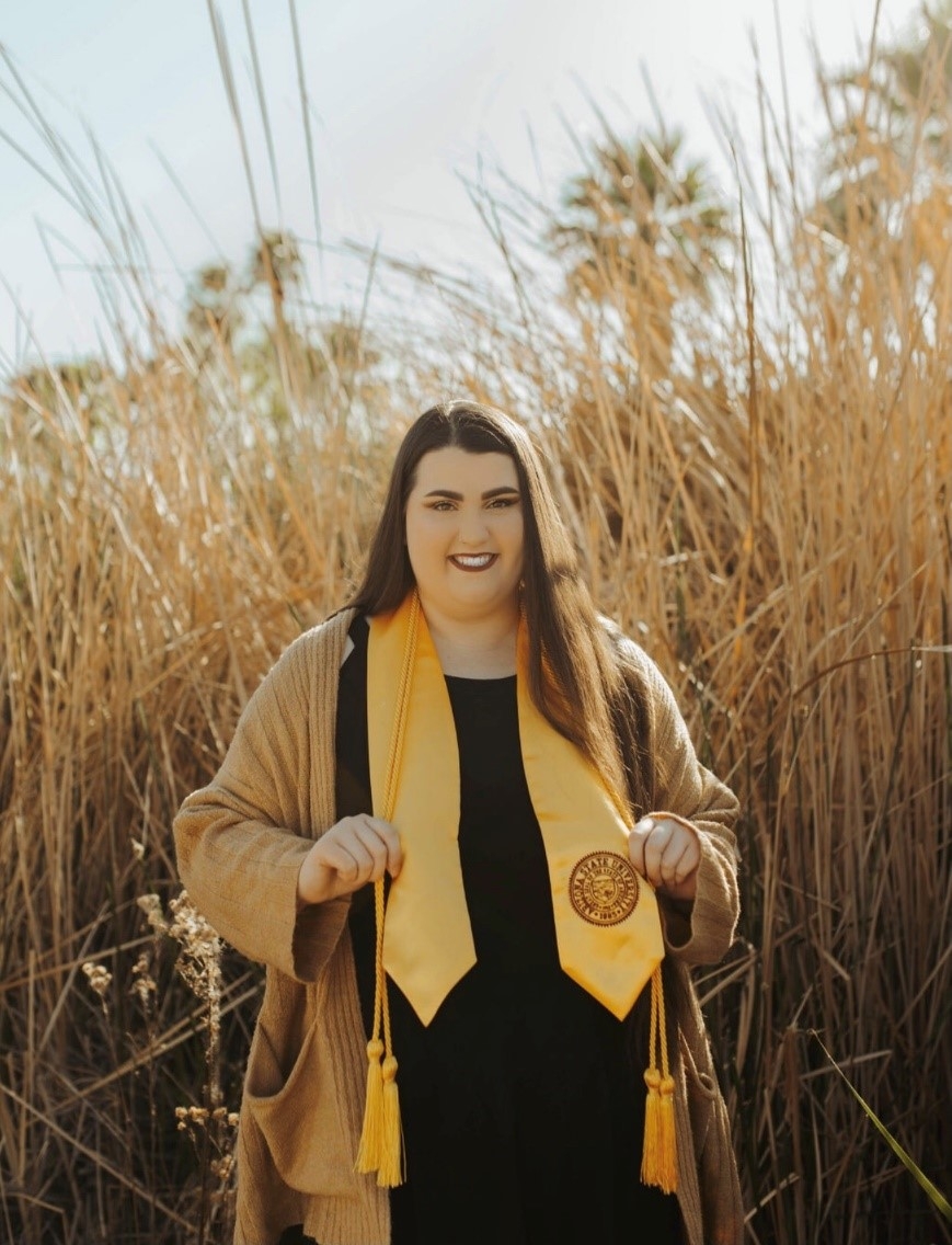 Desiree Melvin standing in a field in her graduation robe and stole