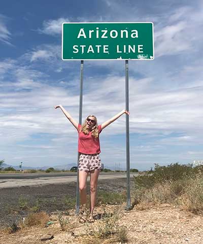 ASU honors student Emily Hagood strikes a happy pose next to an Arizona state line sign on the highway