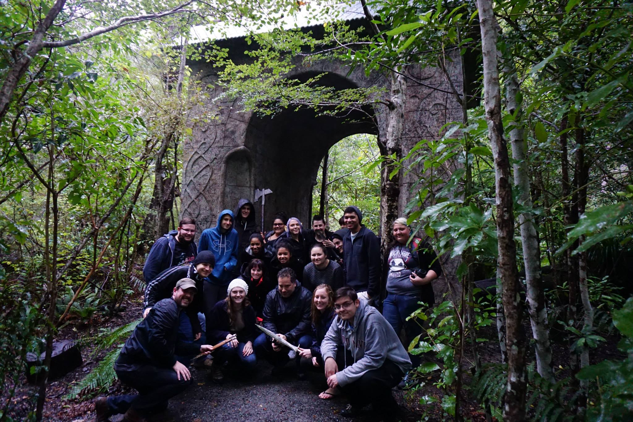 A group stands in front of a stone arch in a forest.