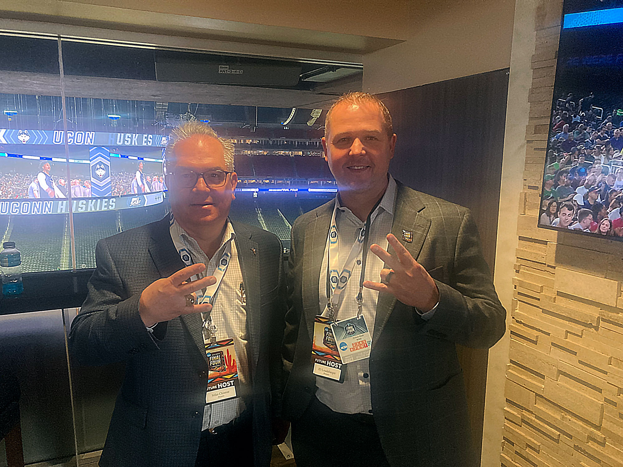 Two men in Final Four suite flashing pitchforks with hands