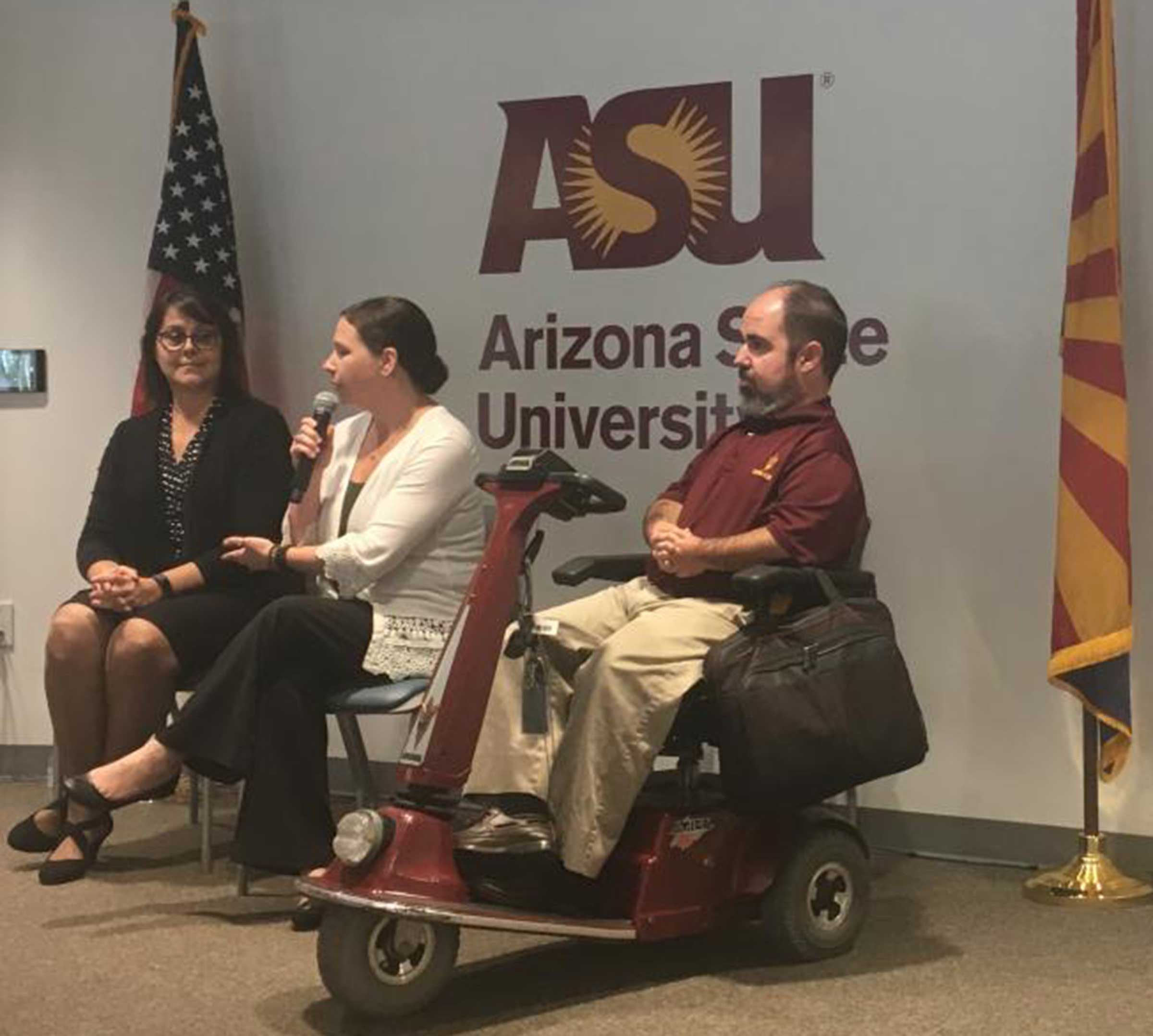 A man in an electric wheelchair sits by two women in front of an ASU logo