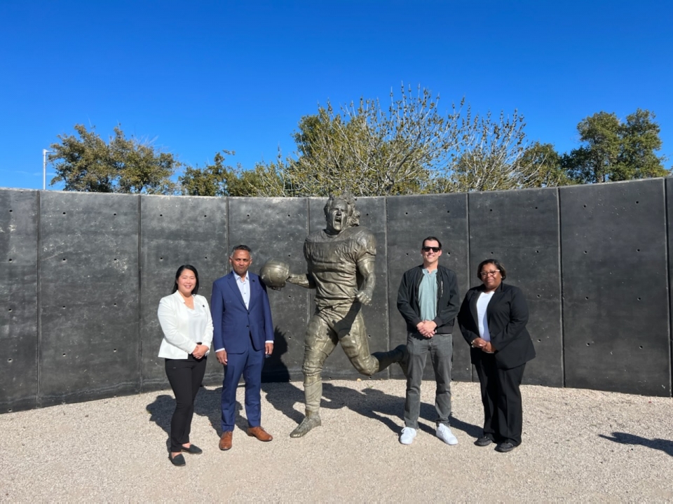 Four people posing for a photo next to a statue of a football player in an outdoor setting.