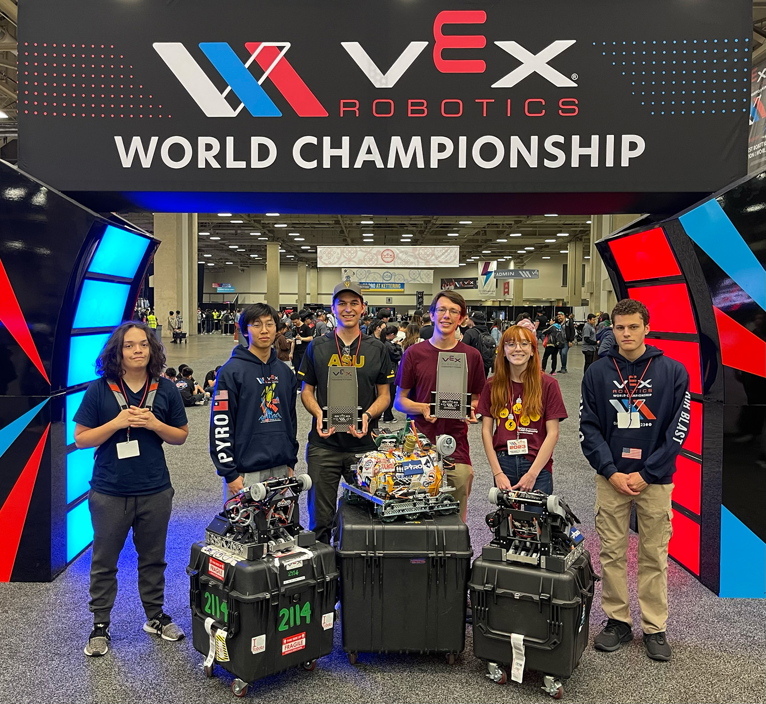 Rossum Rumblers PYRO team members Armando Pinedo, Brian Hou, Charles Jeffries, Kenneth Hodson, Kylie Baker and Andrew Ayerh stand in front of an arch with their robots and awards at the 2023 VEX Robotics World Championship