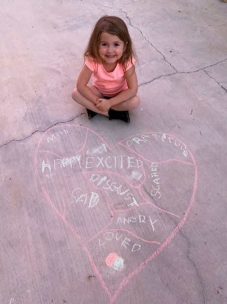 young girl sitting on sidewalk next to heart drawn with chalk