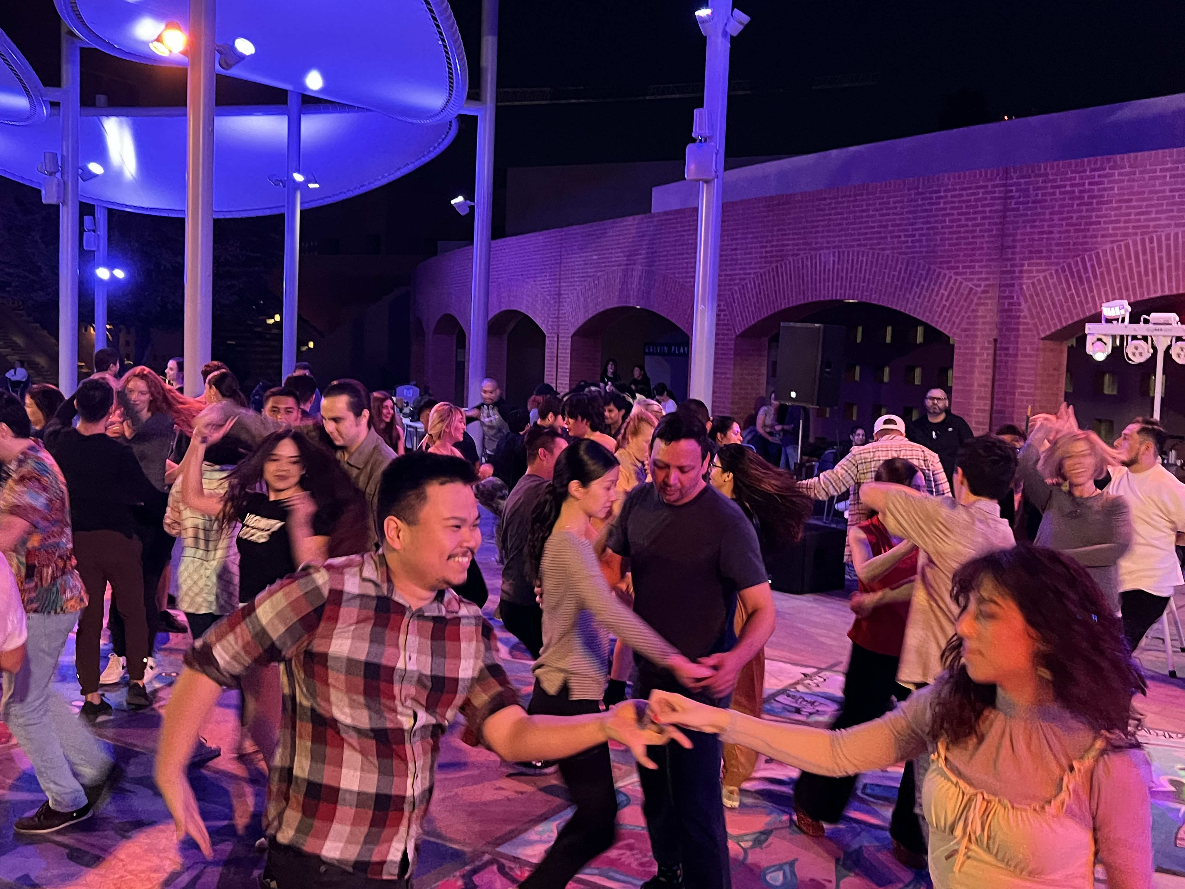 Students dance salsa outside under the colored lights at Nelson Fine Arts Plaza