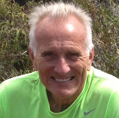 Emeritus Professor Lee Croft smiles for a photo while traveling in Hawaii. He has white hair and is wearing a neon green T-shirt. Behind him is island foliage.
