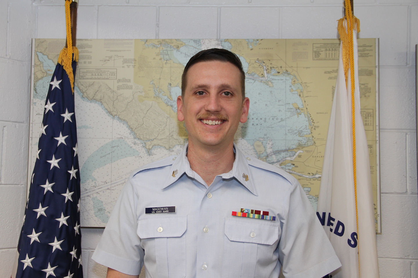 ASU grad  wearing his Navy uniform in front of a map and standing next to an American flag.