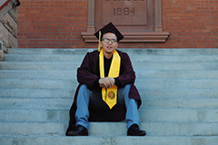 man in graduation cap and gown sitting on steps in front of Old Main