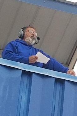 Man wearing a headset looking out at a football field.