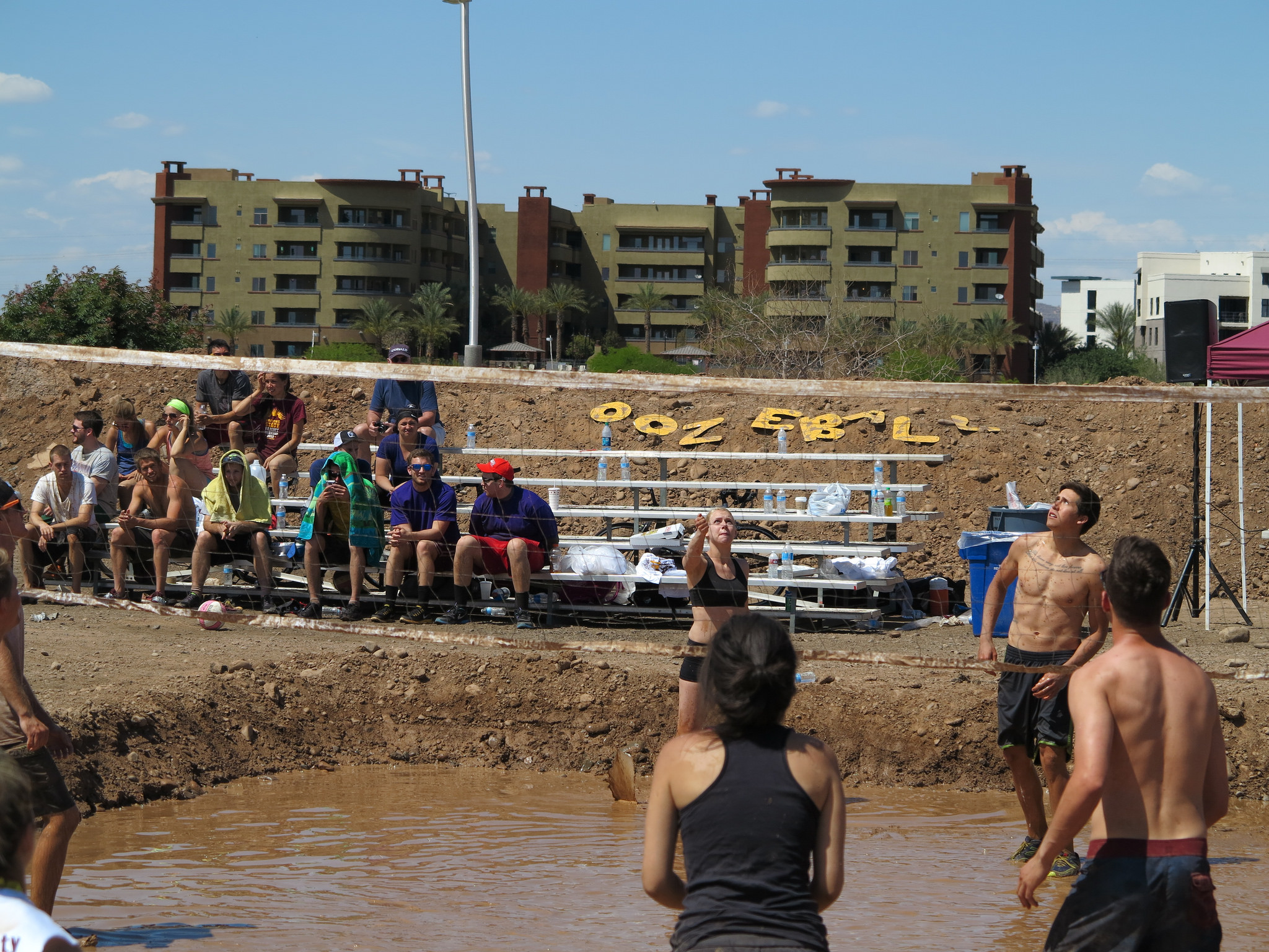 people watching students playing mud volleyball from bleachers