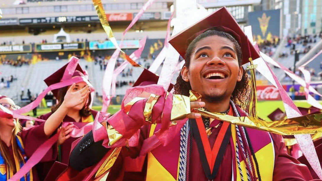 ASU grad  wearing a maroon cap and gown at a graduatino ceremony.