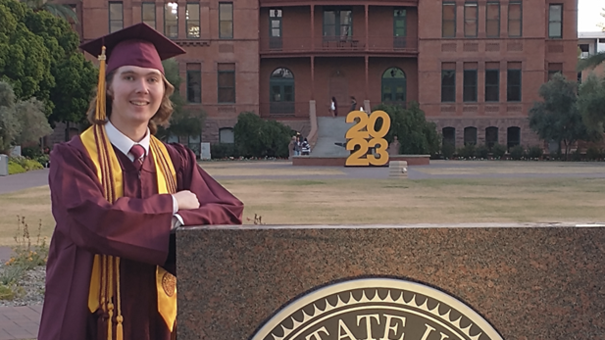 Student in cap and gown posing in front of ASU building