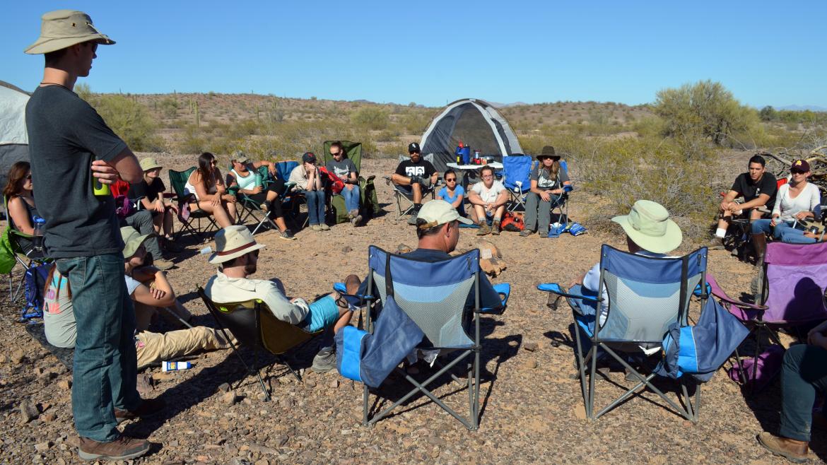 Students sit in a circle in the desert on a biology camping trip.