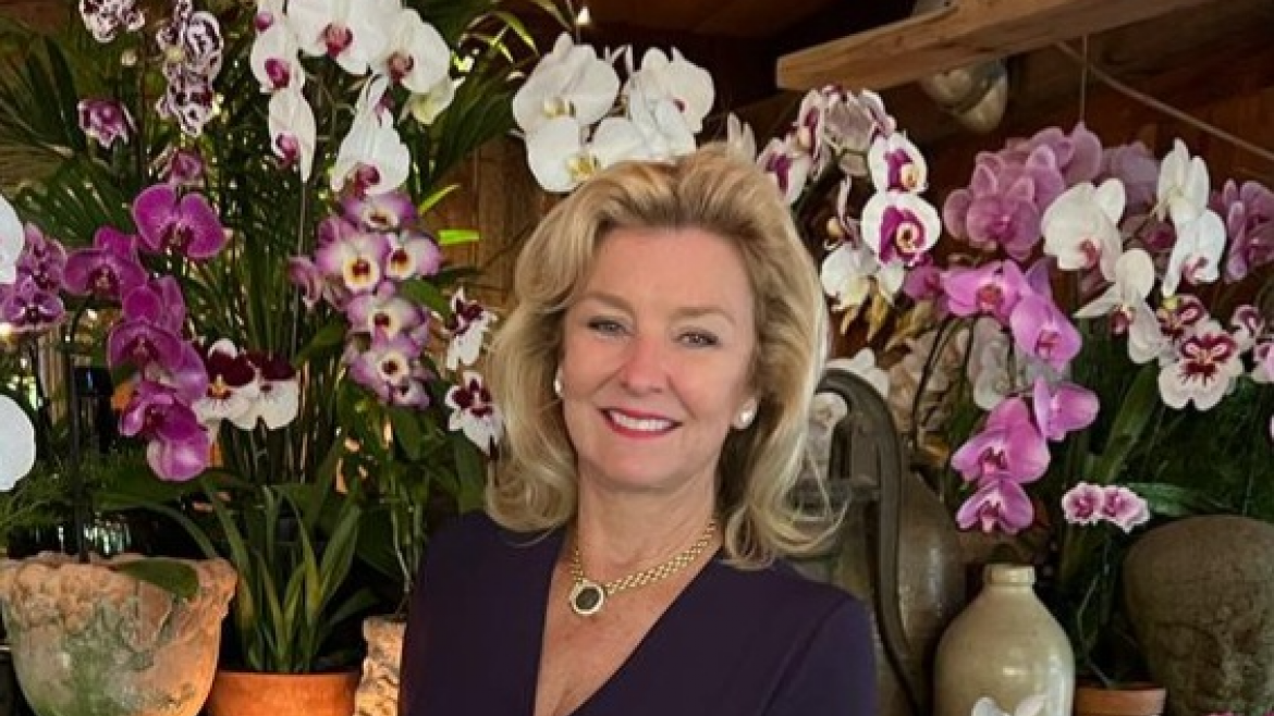 Woman smiling in front of a backdrop of flowers.