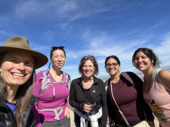 Nancy Grimm and ESSA (Earth Systems Science for the Anthropocene) scholars smile against a blue sky background while on a hike. 